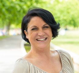 Cheerful excited woman walking in park and laughing. Mature black haired lady enjoying nature outdoors and smiling at camera. Happy woman outdoors concept